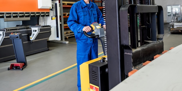 Een werknemer in een magazijn gebruikt een handpalletstapelaar om pallets te vervoeren.