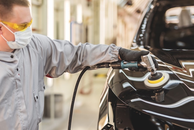 Een werknemer van een autofabriek in handschoenen en een medisch masker polijst het oppervlak