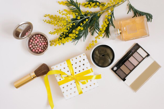 Een werkruimte met gele mimosa bloemen decoratieve cosmetica een geschenkdoos met een strik op een witte achtergrond Plat leggen Bovenaanzicht vrouwelijke blogger achtergrond