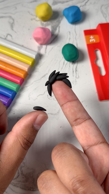 Een wijsvinger versierd met zwarte plasticine die haar simuleert Fijnmotorische vaardigheden met klei