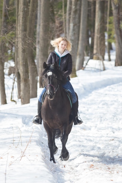 Een winterbos een jonge blonde vrouw rijdt op een paard op besneeuwde grond