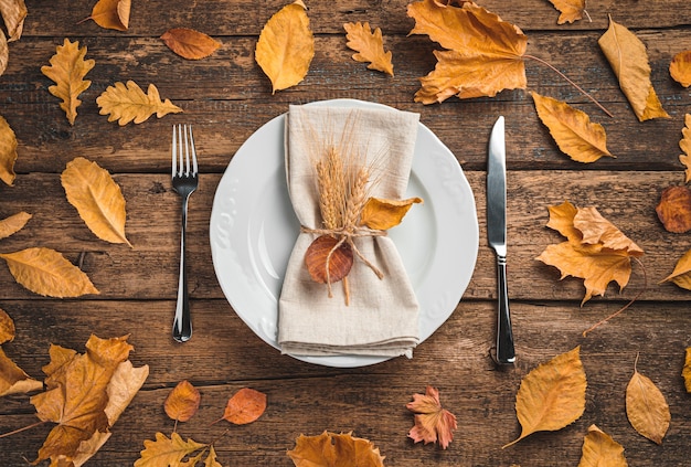 Een wit bord met een servet en bestek op een houten ondergrond met herfstbladeren