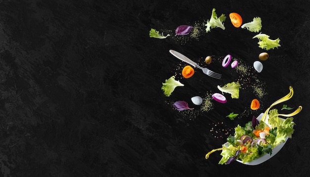 Een wit bord met salade en zwevend in de lucht ingrediënten: olijven, sla, ui, tomaat, mozzarellakaas, peterselie, basilicum en olijfolie. Kopieer ruimte.