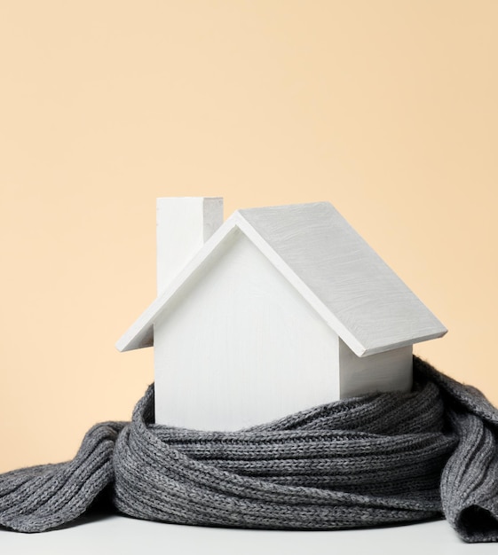Een wit houten miniatuurhuisje gewikkeld in een grijze gebreide sjaal. Isolatieconcept voor gebouwen, leningen voor reparaties