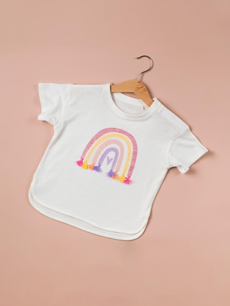Een wit kinder39s T-shirt met een regenboog op een hanger op een roze achtergrond Kleding voor een meisje