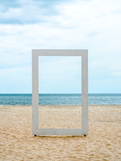 Een wit leeg houten frame dat door kan kijken naar het zeegezicht, het strand, de zee en de blauwe lucht, minimale stijl, verticale stijl.
