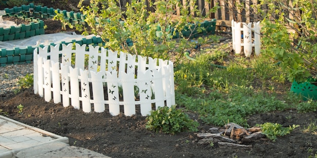 Een wit plastic hek rond een bloembed. Tuindecoratie in het vroege voorjaar.