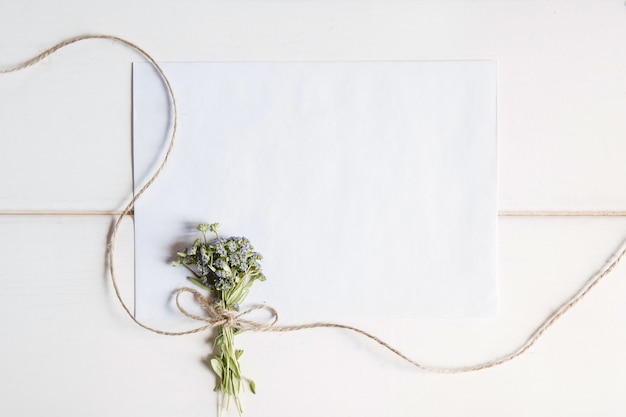 Een witte blanco envelop met een klein boeketje wilde bloemen vastgebonden met touw op een wit houten oppervlak