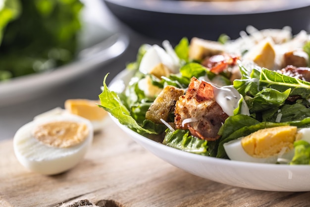 Een witte bowl vol Cezar salade met croutons spek en Parmezaanse kaas