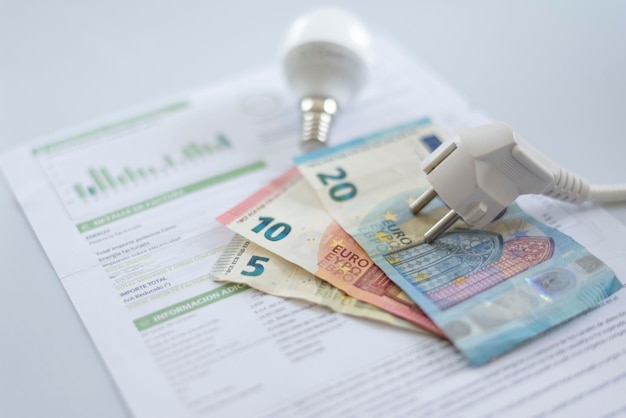 Een witte elektrische dop, een gloeilamp en eurobankbiljetten op een elektriciteitsrekening. Verhoging van elektriciteit