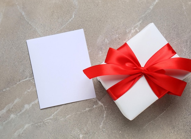 Een witte geschenkdoos met een rood lint en een witte kaart aan de bovenkant.