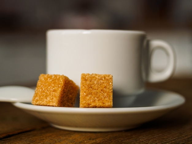 Een witte kop koffie en twee blokjes gele suiker.