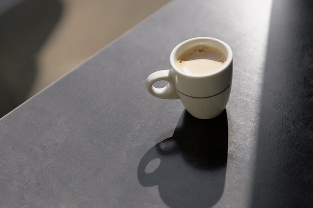 Een witte kop koffie met harde schaduwen op de grijze achtergrondkleur van de tafel. Ochtend koffie concept