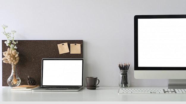 Een witte laptop met leeg scherm zet op een wit bureau omgeven door kantoorapparatuur.