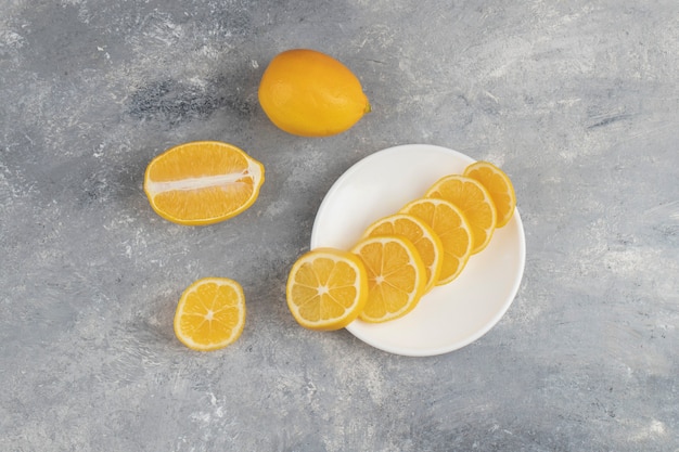Een witte plaat met plakjes verse citroen op een marmer.