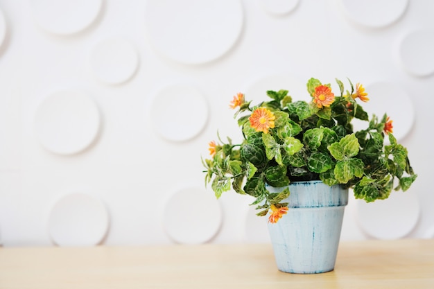 Een witte pot met oranje bloemen geplaatst op een houten tafel met een witte achtergrond.