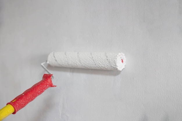 Een witte roller op een lang rood handvat schildert de muur witte horizontale formaatplaats voor tekstsjabloonachtergrond