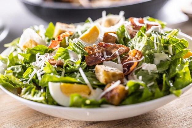 Foto een witte schaal vol cezar salade met croutons bacon en parmesan kaas close up