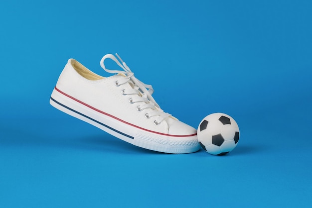 Een witte sneaker en een kleine voetbal op een blauwe achtergrond