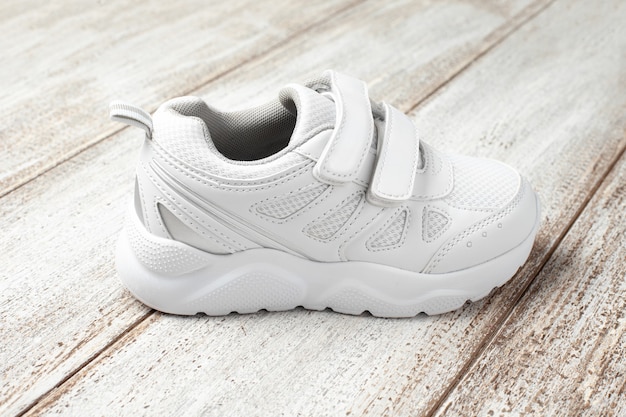 Een witte sneaker op een lichte achtergrond een kinderleer met stoffen sportsneaker met klittenbandsluiting...