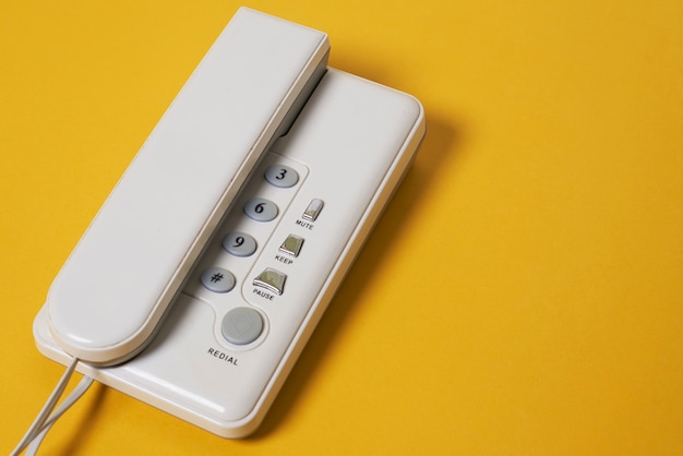 Een witte vaste telefoon met draad op geel