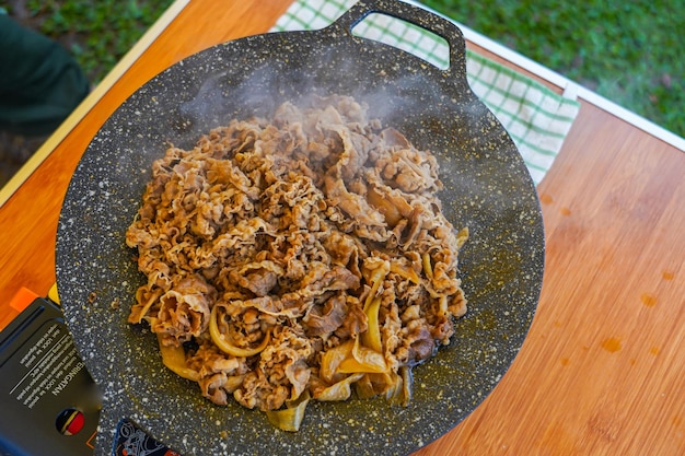 Een wok met daarop een kom rundvlees en uien.