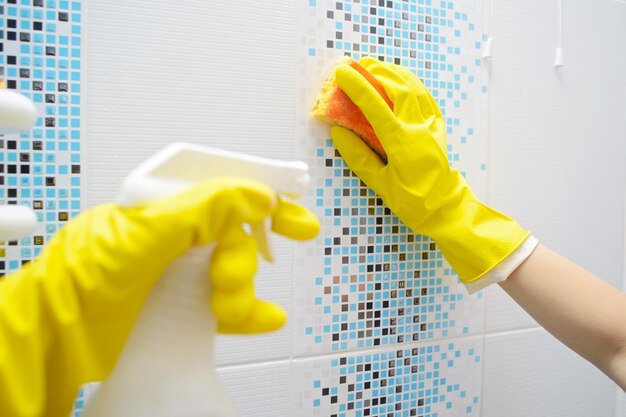 Een wooman-wasmachine maakt het betegelde oppervlak in de badkamer schoon Het meisje houdt een reinigingsspray en een spons in zijn handen Ruimte kopiëren