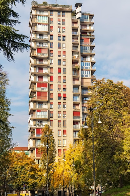 Een woongebouw met meerdere verdiepingen in de stad tussen groene bomen tegen een lichtblauwe hemelachtergrond