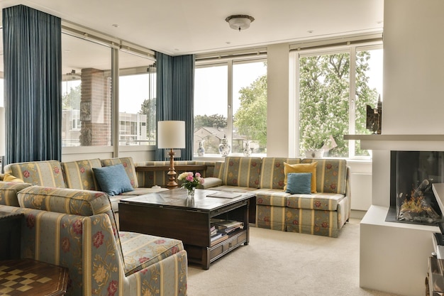 een woonkamer met bankjes stoelen en een open haard in het midden van de kamer is grote ramen