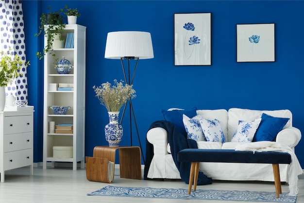 Een woonkamer met een blauw-witte bank en een witte plank met daarop een vaas met bloemen.