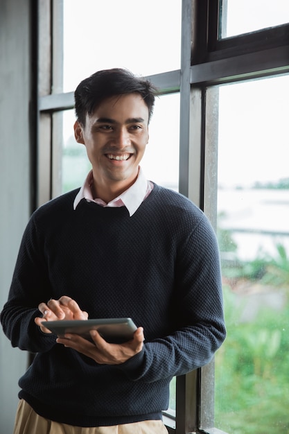 Een zakenman die digitale tablet houdt bekijkt de camera vooraan de vensters