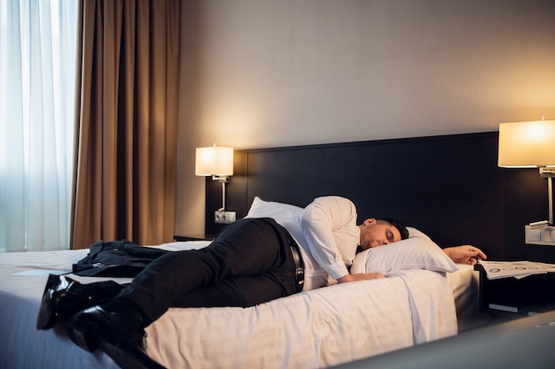Een zakenman die op een bed in een hotelruimte ligt