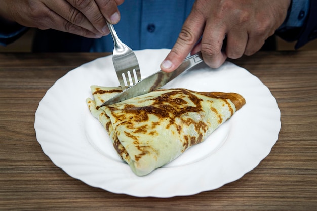 Een zakenman eet een pannenkoek tijdens een lunchpauze in een restaurant. man met een lepel en een vork in zijn handen bereidt zich voor op ontbijt of lunch, eten op tafel