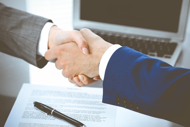 Een zakenman en een zakenvrouw schudden elkaar de hand boven het ondertekende contract.