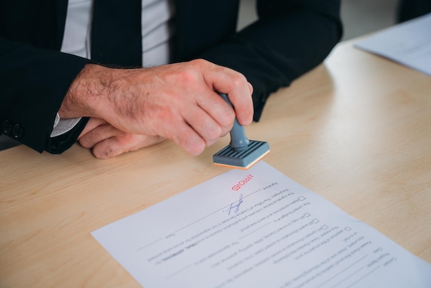 Een zakenman stempelt met de hand een goedgekeurd stempel op een tekstdocument aan een tafel met een contract