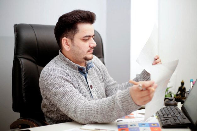 Een zakenman zit op een stoel in kantoor en houdt papier in handen.
