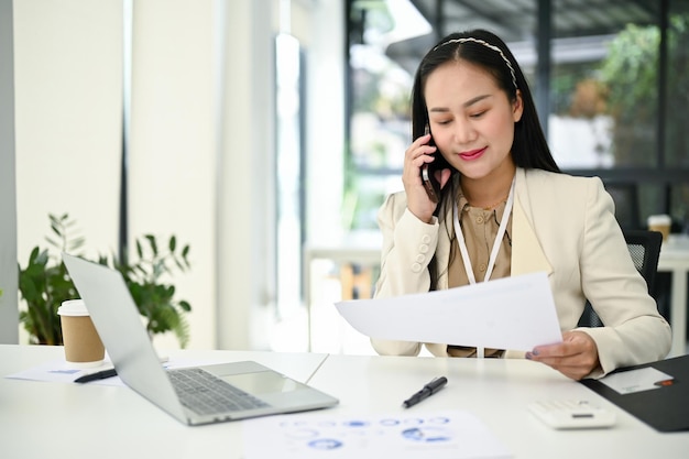 Een zakenvrouw die aan de telefoon praat met haar zakelijke klant aan haar bureau