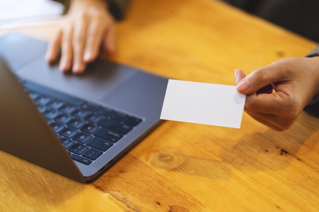 Een zakenvrouw die blanco visitekaartjes vasthoudt en geeft tijdens het gebruik van een laptopcomputer op kantoor