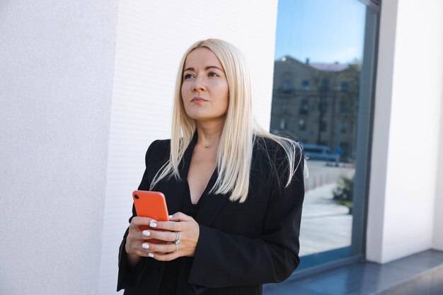 Een zakenvrouw in een stijlvol pak met een telefoon poseert op straat