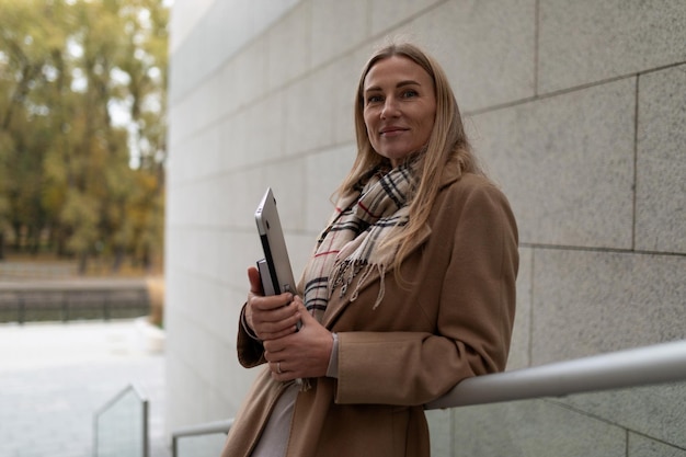 Een zakenvrouw staat bij een zakencentrum met een laptop en kijkt rechtstreeks naar de camera