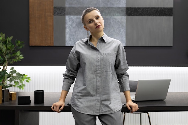 Een zakenvrouw staat leunend op een tafel tegen de achtergrond van een modern, stijlvol kantoor