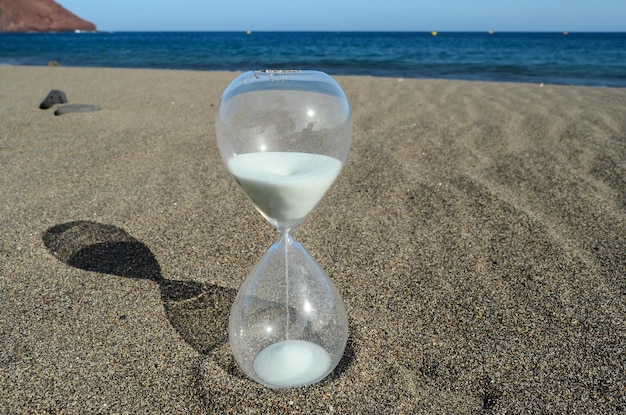 Een zandloper op het zandstrand in de buurt van het Ocean Time-concept