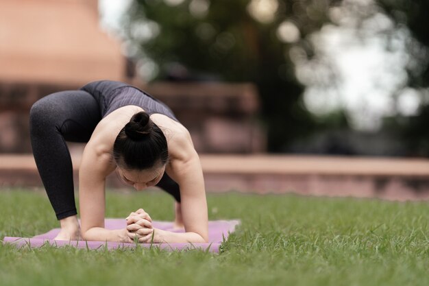 Een zelfverzekerde Aziatische vrouw in sportoutfit die yoga doet buiten in het achtertuinpark