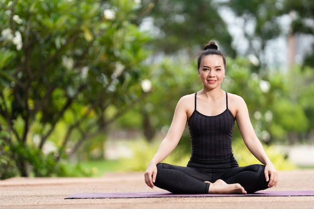 Een zelfverzekerde Aziatische vrouw van middelbare leeftijd in een sportoutfit die 's ochtends yogaoefeningen doet op de yogamat buiten in de achtertuin. Jonge vrouw doet yoga-oefening buiten in het openbare natuurpark
