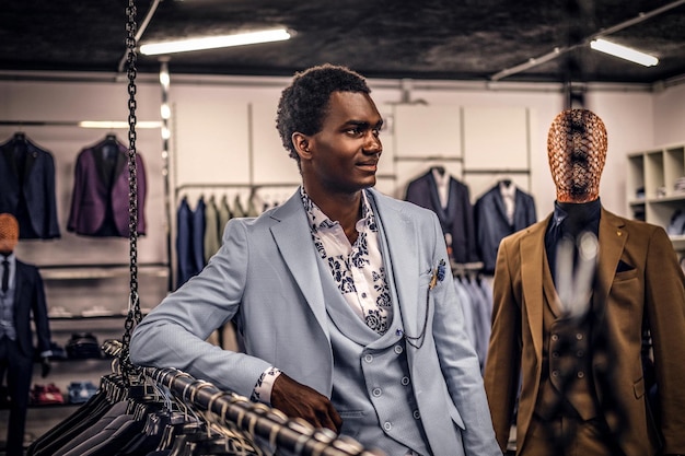 Een zelfverzekerde elegant geklede Afro-Amerikaanse man leunend op een mannequin in een klassieke herenkledingwinkel.