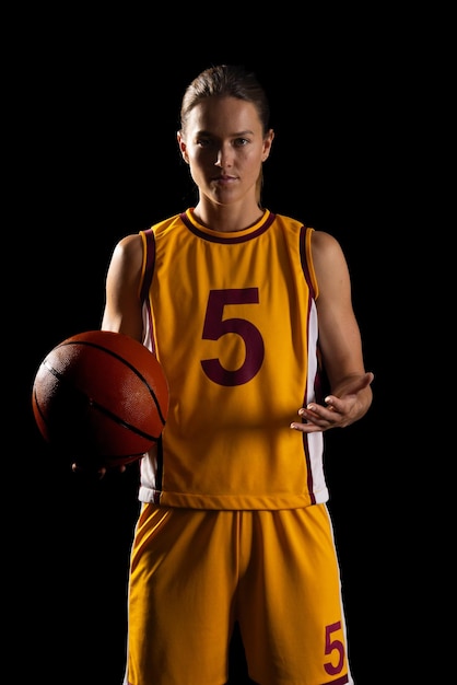 Een zelfverzekerde jonge blanke vrouwelijke basketbalspeler poseert in een basketbaluniform op een zwarte achtergrond