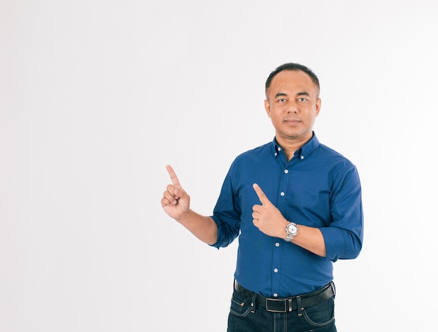Een zelfverzekerde senior Aziatische man in een blauw zakelijk casual shirt dat staat en met zijn vingers in de lucht wijst met kopieerruimte. Isoleer op witte achtergrond.