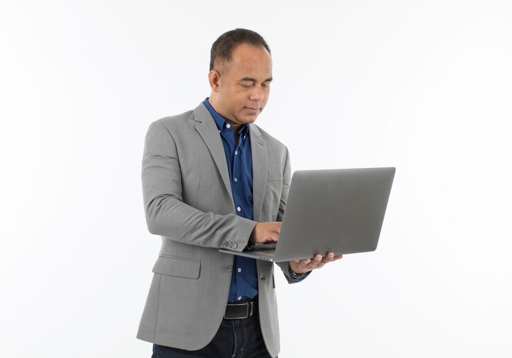 Een zelfverzekerde senior Aziatische man van middelbare leeftijd in een blauw zakelijk casual shirt met een grijze jas die de laptopcomputer vasthoudt. Isoleer op witte achtergrond.