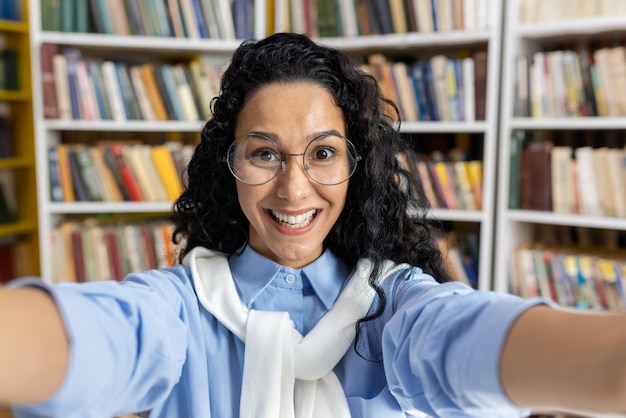 Een zelfverzekerde Spaanse student maakt een selfie omringd door boeken in een bibliotheek.