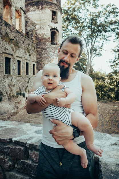 Een zes maanden oude baby in de armen van een vader tegen de achtergrond van een oud kasteel